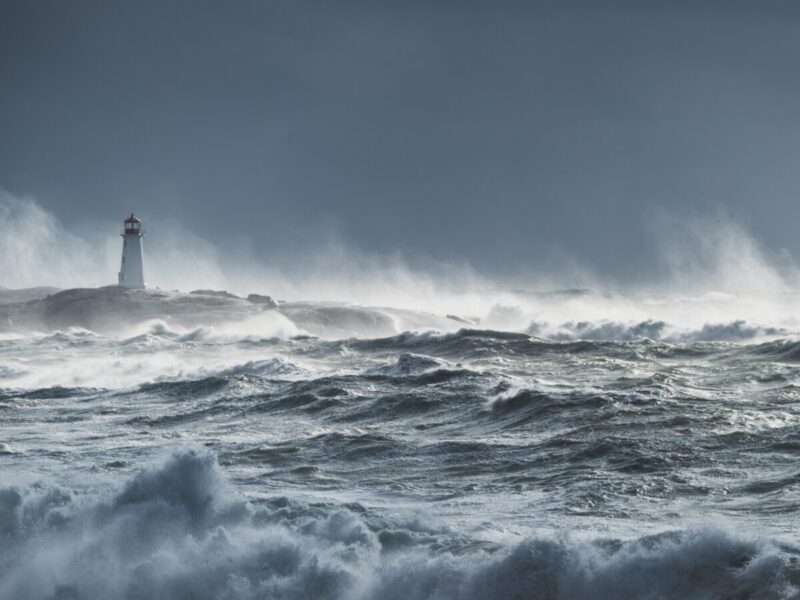 A seascape with waves crashing on a white and red lighthouse on the left.