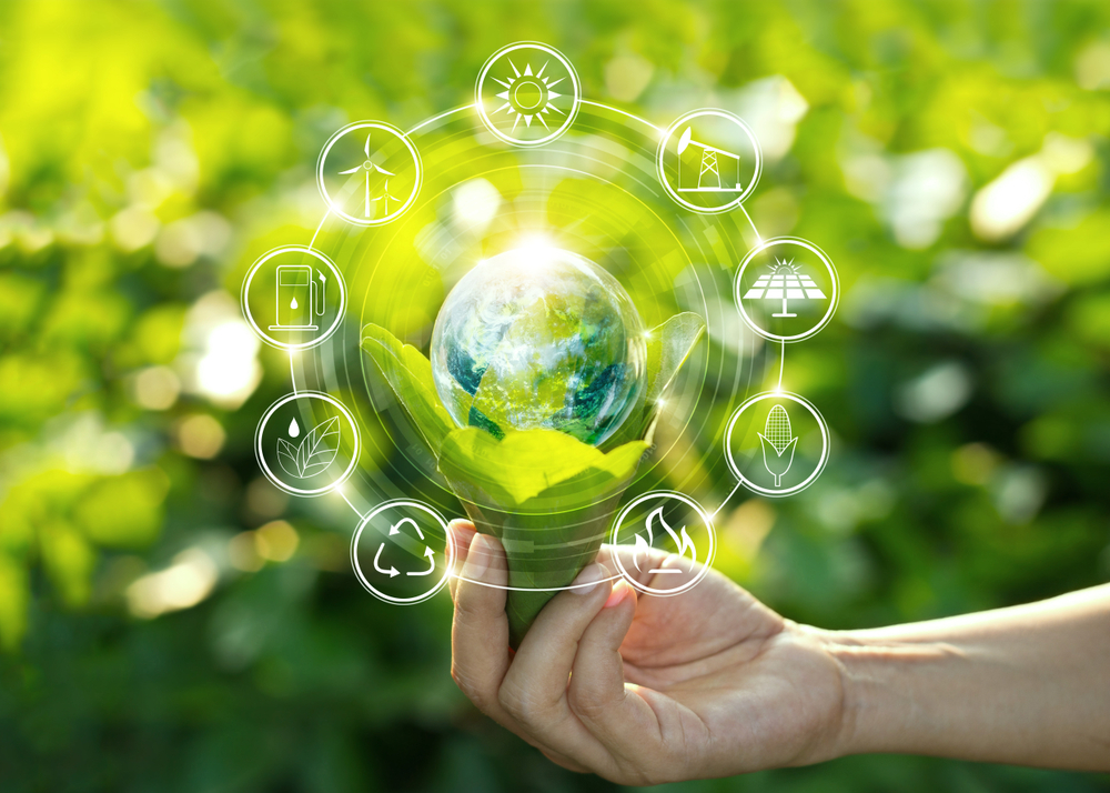 An image to depict sustainability: a hand holds a bouquet of leaves in which a globe of Earth resets. Around the globe are icons depicting: a petrol pump, a windfarm, the sun, an oil pump, a solar panel, an ear of corn, a fire, a triangle recycling symbol, and a plant being watered.