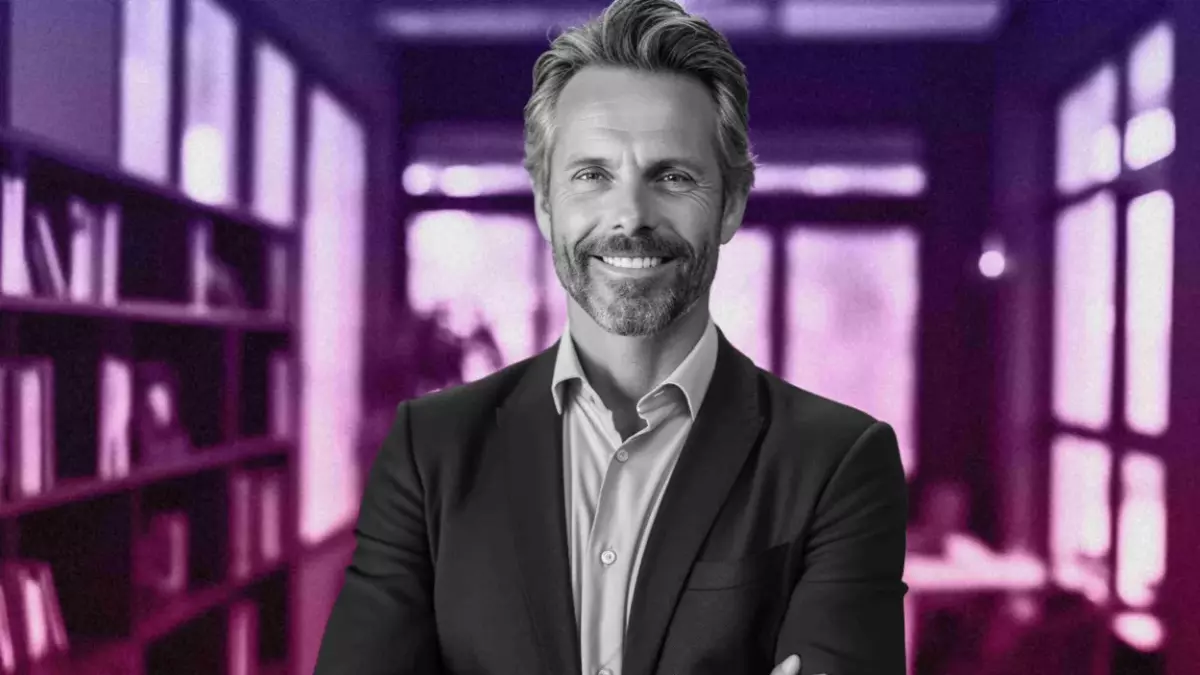 Adobe Stock/Enrique] A photo of a smiling middle aged white in business dress posing in front of a desk a book shelf.