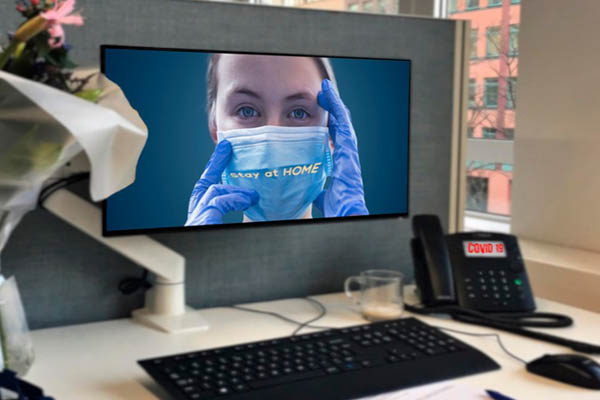 A photo of an office desk with an image on the computer monitor of a nurse in a mask and the phrase, "stay at home" across her mask.