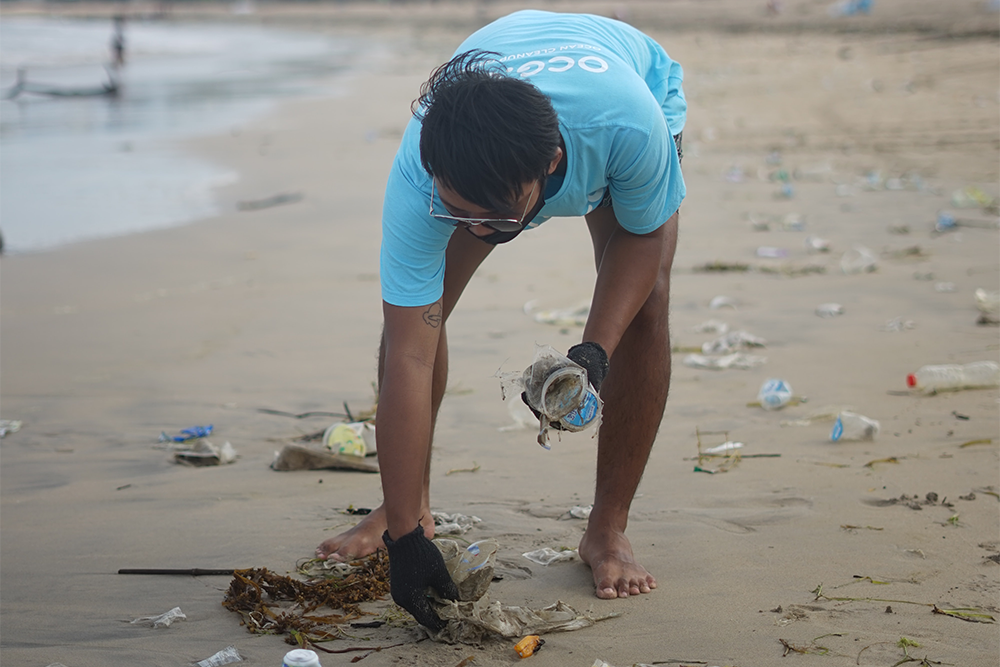 A photo of a male volunteer picking up trash from a littered beach.