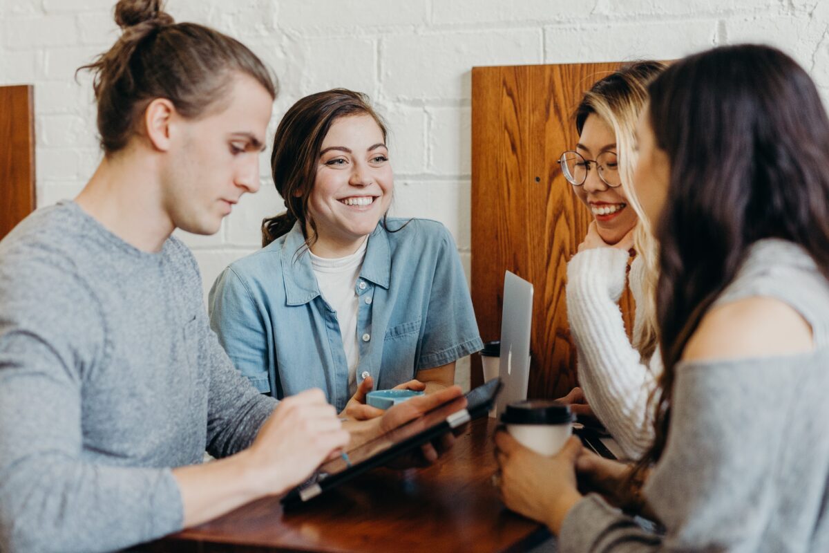A diverse group of Millennial employees sit at a table, smiling and discussing work.