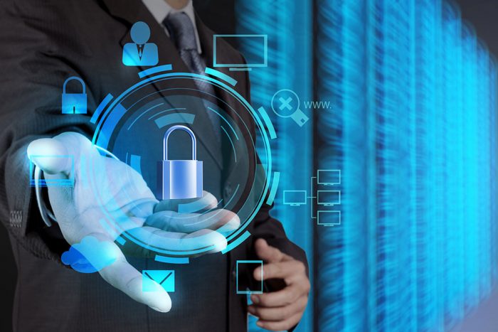 The image is a photo of a businessman holding a padlock on a virtual screen. The padlock is a symbol of security and privacy. It is often used to represent cybersecurity and data protection