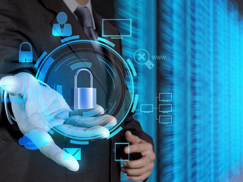 The image is a photo of a businessman holding a padlock on a virtual screen. The padlock is a symbol of security and privacy. It is often used to represent cybersecurity and data protection