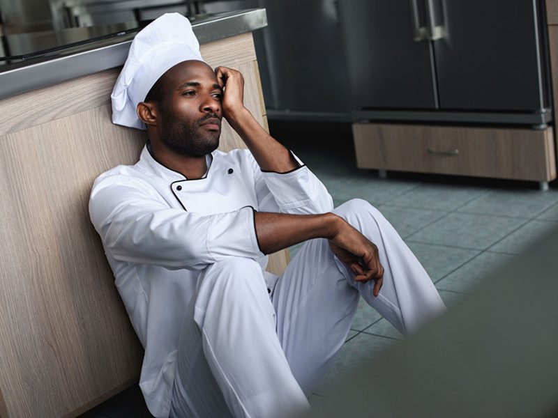 a black man working as chef sitting on a kitchen floor