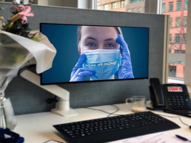 A photo of an office desk with an image on the computer monitor of a nurse in a mask and the phrase, "stay at home" across her mask.