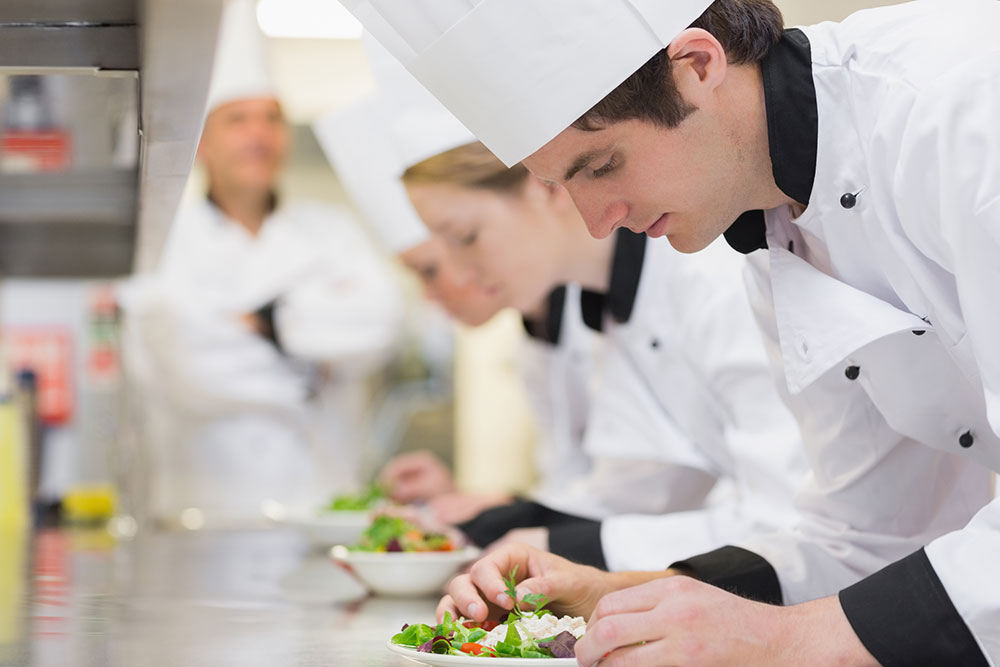 the image is showing three chefs in a kitchen are dressing plates