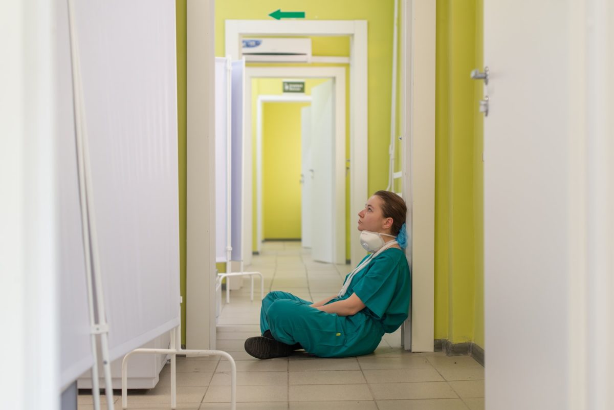 Photo of a female nurse in scrubs slumped in a hallway from tiredness